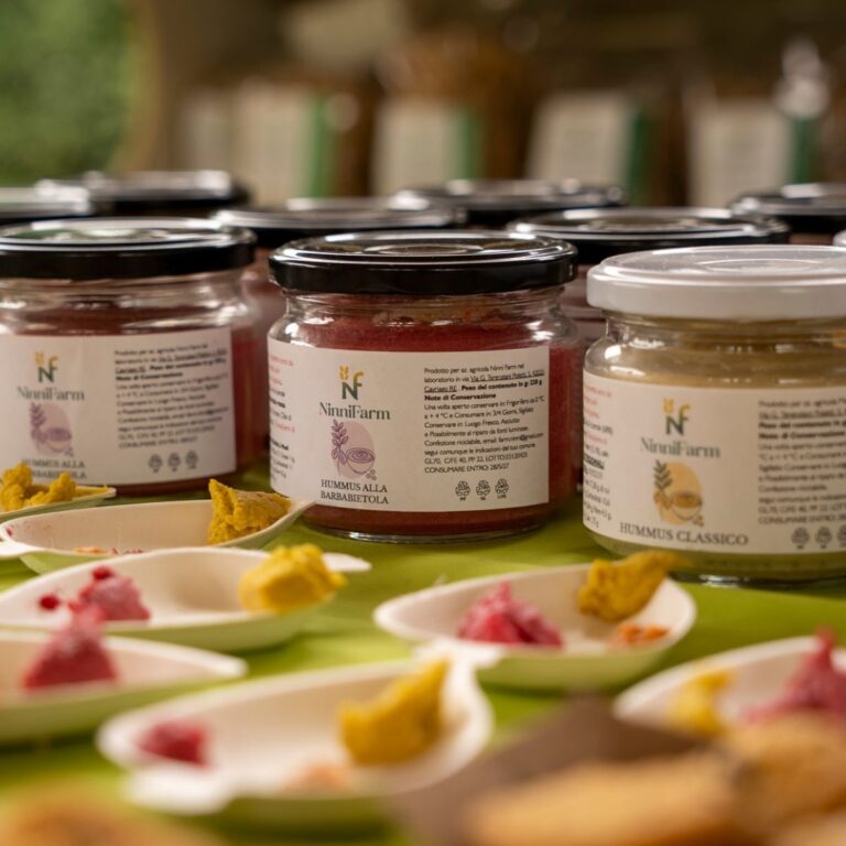 Barattoli in vetro di hummus alla barbabietola e hummus classico NinniFarm con pirottini di degustazione in primo piano.