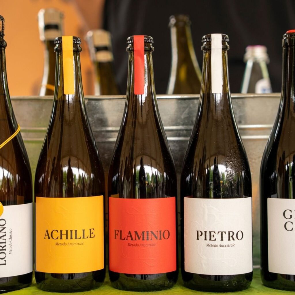 Primo piano delle bottiglie di vino Cantina Roncaglia: Achille, Flaminio e Pietro a Metodo Ancestrale con etichette colorate.