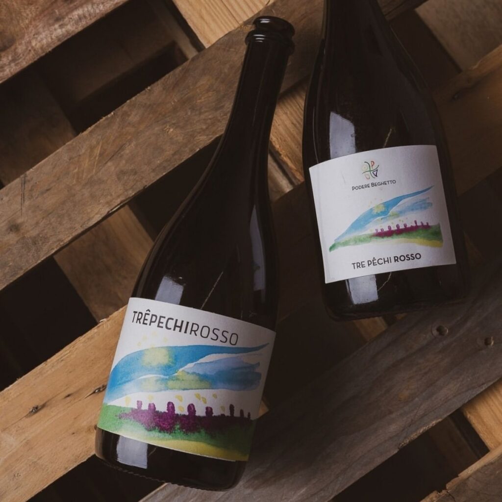 Due bottiglie di vino Trêpêchirosso di Podere Beghetto con etichetta ad acquerello appoggiate su una struttura in legno.