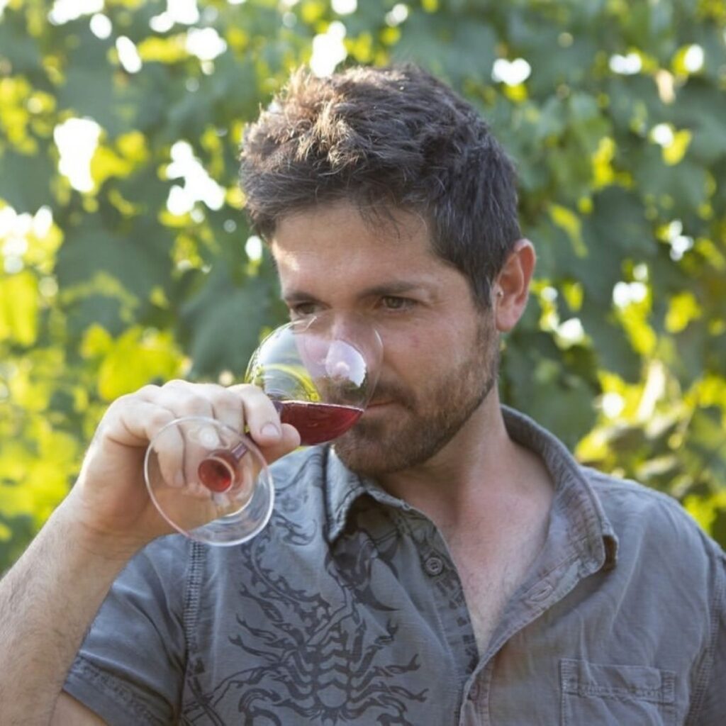 Il produttore di Podere Beghetto mentre valuta i profumi di un calice di vino rosso immerso tra le vigne.