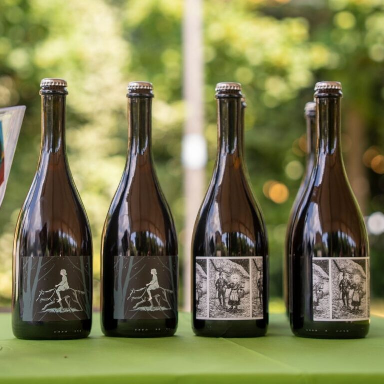 Quattro bottiglie di vino biodinamico Terrevive con etichette illustrate in bianco e nero e tappo a corona allineate sullo stand.