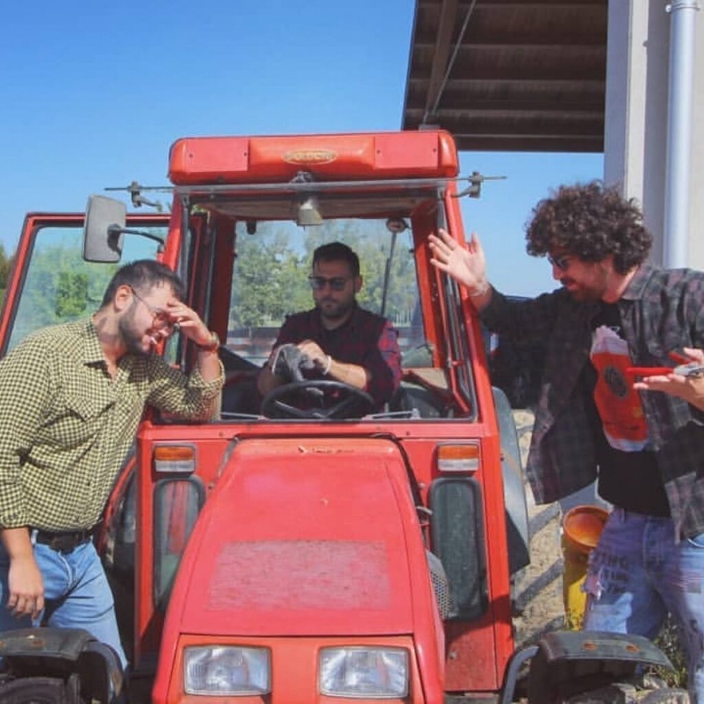 Tre giovani vignaioli di Cantina Bassoli scherzano attorno a un trattore rosso nei vigneti della tenuta.