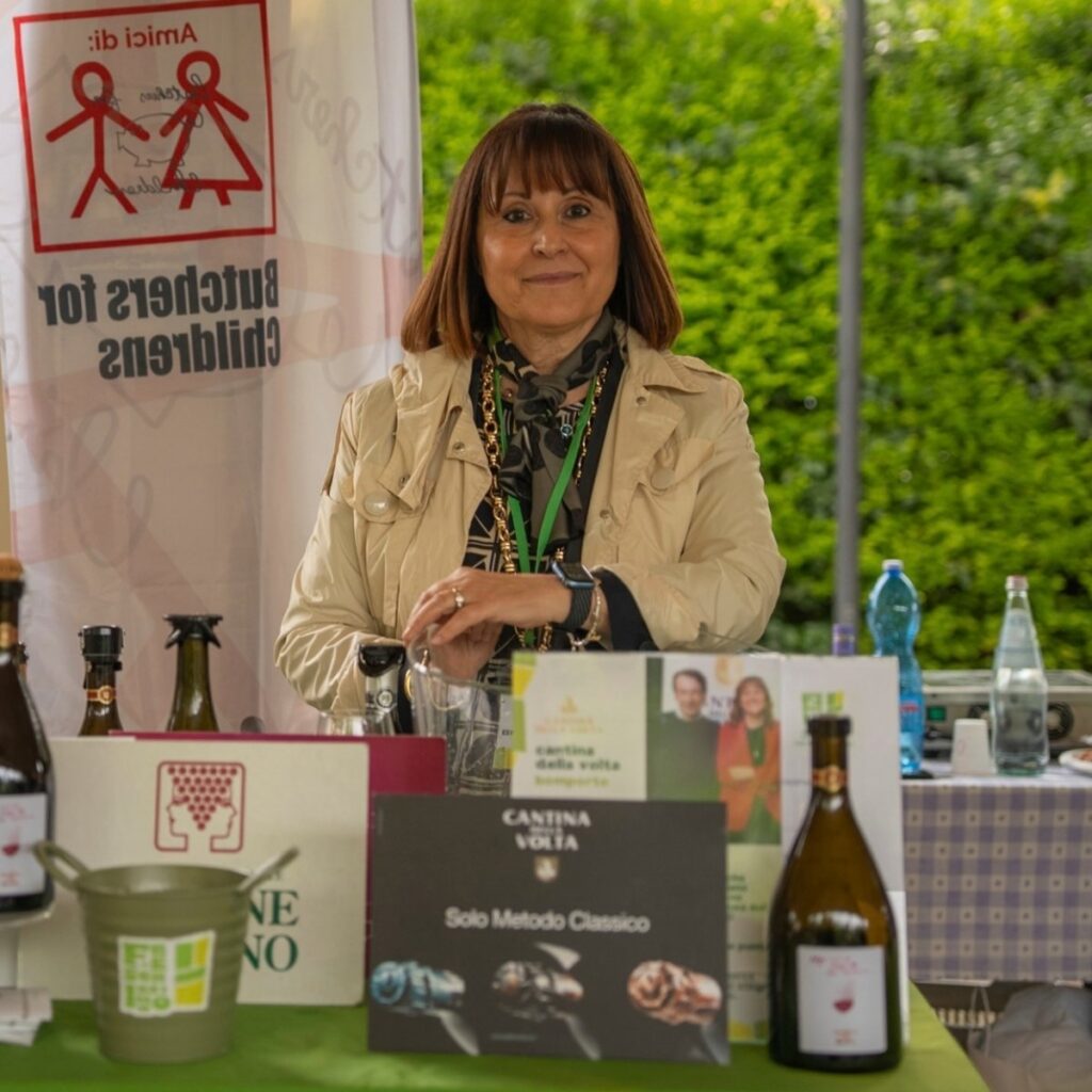 Esponente di Cantina della Volta allo stand promozionale con bottiglie di spumante Metodo Classico e materiale informativo.