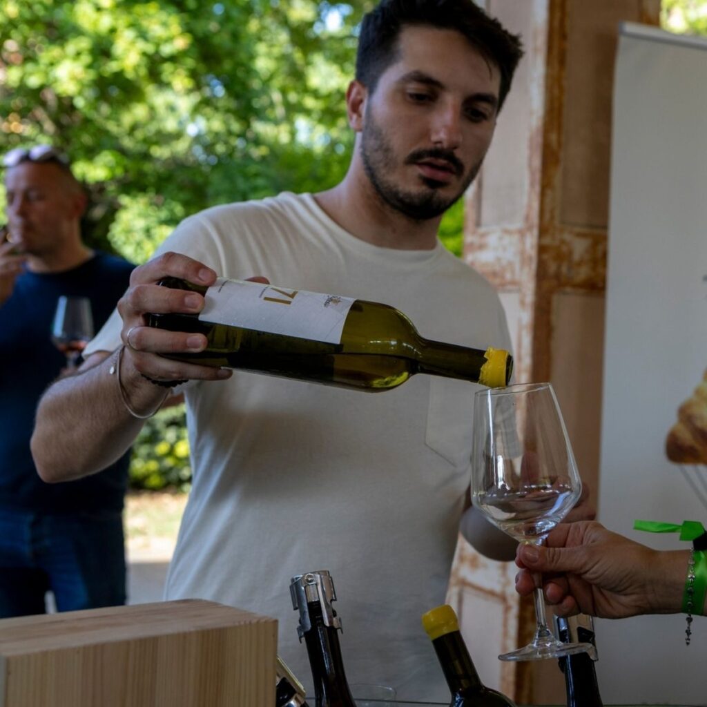 Produttore della Cantina Martinelli in maglietta bianca mentre versa il vino 171 in un calice da degustazione.