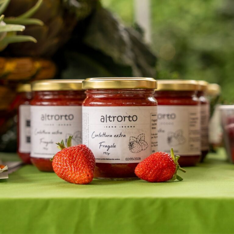Vasetto di confettura extra di fragole Altrorto con due fragole fresche adagiate sul tavolo dello stand.